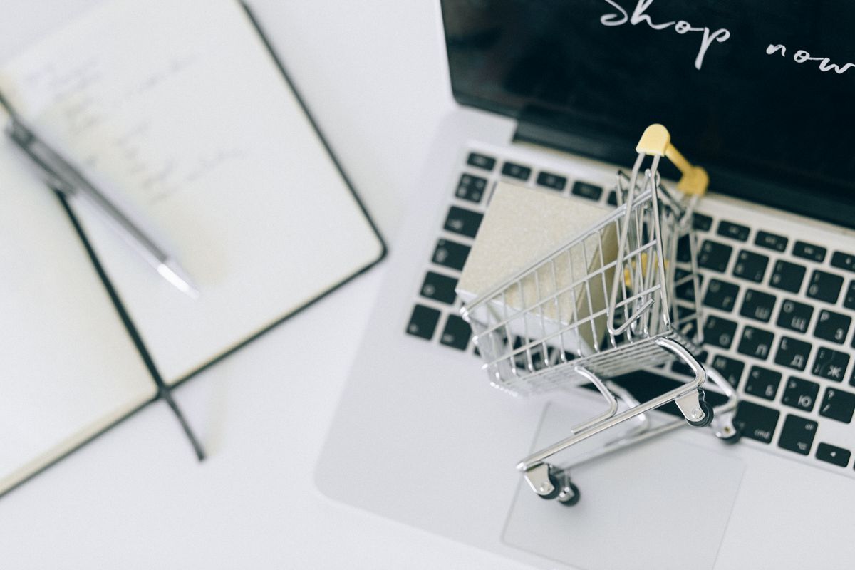 Petit caddie de shopping miniature posé sur le clavier d'un ordinateur portable affichant une boutique en ligne