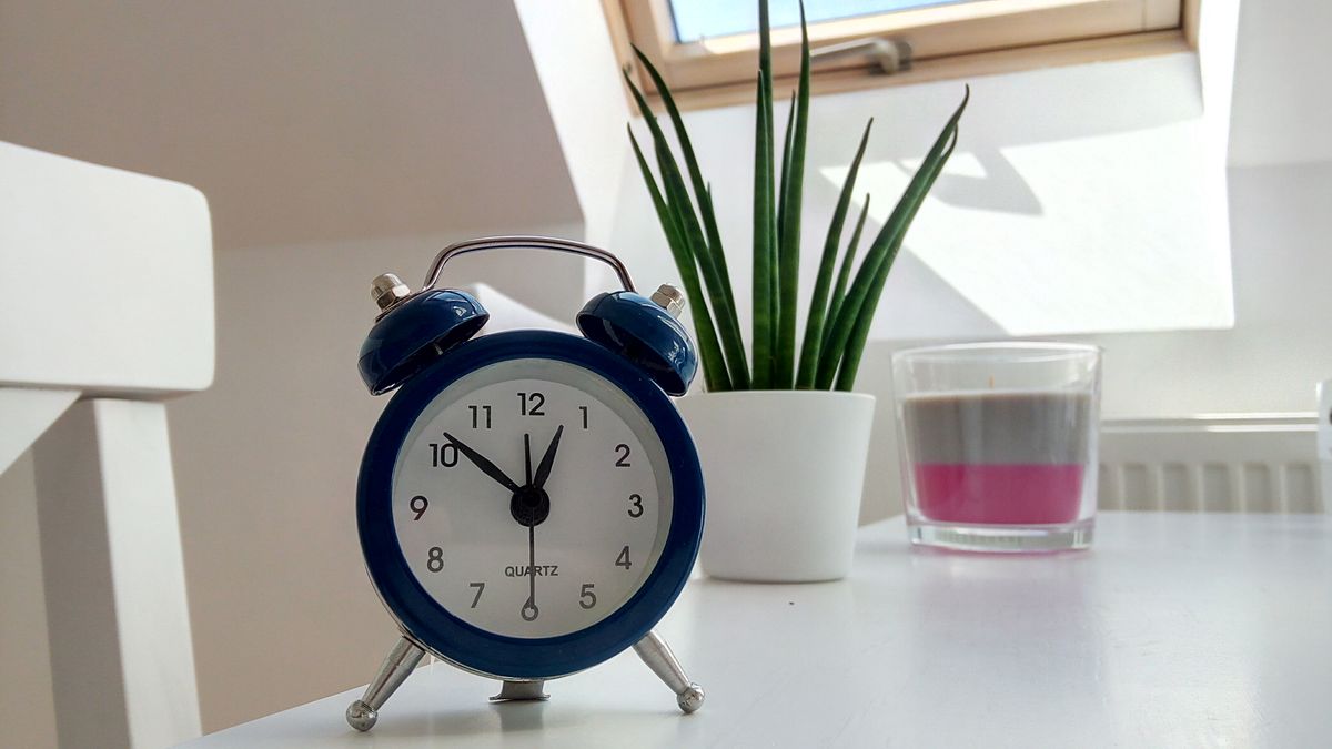 Réveil rétro de couleur bleue posé sur un bureau blanc à côté d'une plante